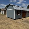 A gray shed with a metal roof in the middle of a field, available for 12x24 Lofted Barns on sale near me.
