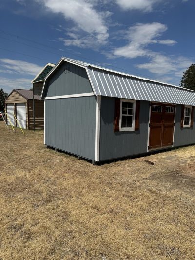 A gray shed with a metal roof in the middle of a field, available for 12x24 Lofted Barns on sale near me.