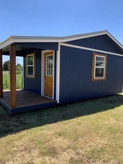 A blue 12x24 Cottage Shed with a wooden porch is available for sale.