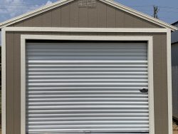 A yard with a 12x20 Garage Shed featuring a roll-up door.