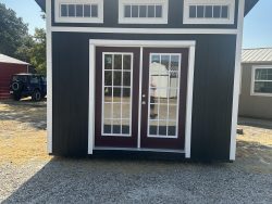A black and white 10x12 Studio Shed with a red door, available on sale at a nearby shed store.