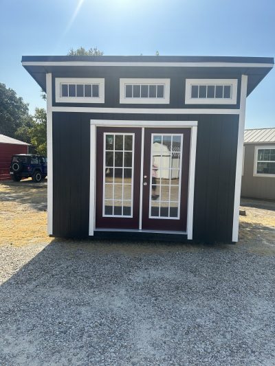 A black and white 10x12 Studio Shed with a red door, available on sale at a nearby shed store.