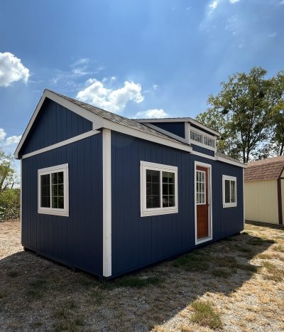 A blue and white 12x24 Chalet Shed, resembling a shed on sale, sitting on a dirt lot.
