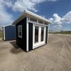 A black and white 8x10 Studio Shed for sale sitting in a parking lot.