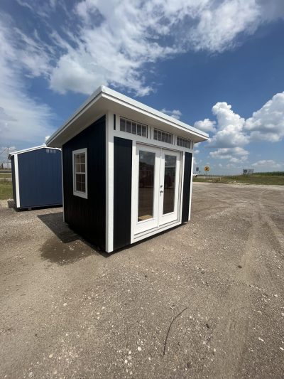 A black and white 8x10 Studio Shed for sale sitting in a parking lot.