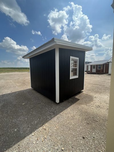 An 8x10 Studio Shed for sale, sitting on a gravel lot.