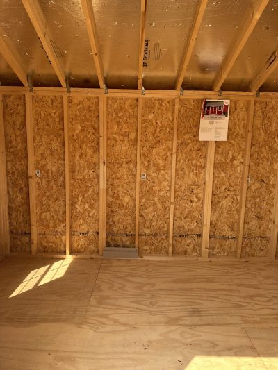 A room with wood flooring and a sign on the wall advertising 8x12 Garden Sheds for sale.