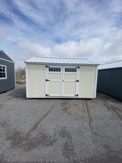 Two 10x14 Utility Sheds for sale in a parking lot.