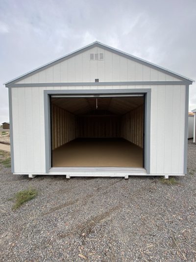 A 16x28 Garage Style Shed for sale with a door in the middle of a gravel lot.