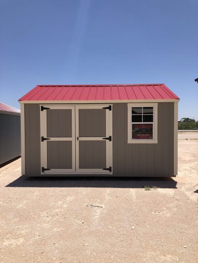 A 10x14 Utility Shed with a red roof available for sale, sitting on a dirt lot.
