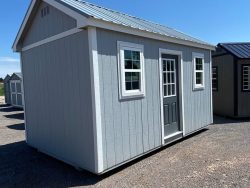 Two 10x16 Chalet Sheds on sale sitting in a gravel lot.
