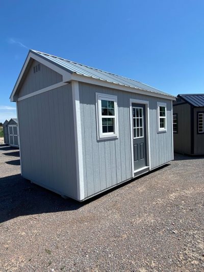 Two 10x16 Chalet Sheds on sale sitting in a gravel lot.