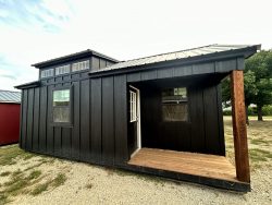 A black 12x24 Chalet Shed, sitting on a dirt lot, also functionally used as a shed on sale.