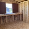The inside of an 8x16 Studio Shed with wood flooring and a window is available for sale.