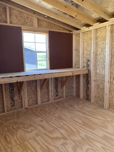 The inside of an 8x16 Studio Shed with wood flooring and a window is available for sale.