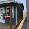 A small gray house adorned with a sign on the front porch, offering 14x28 Cottage Sheds for sale.