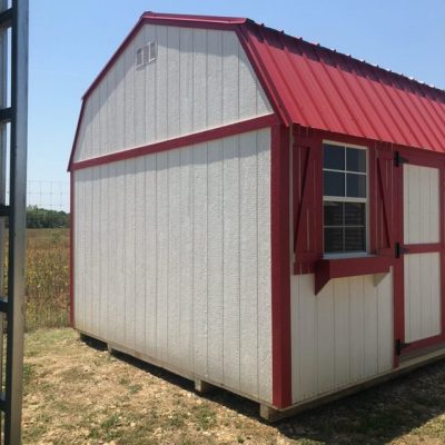 A red and white 12x16 Lofted Barn sitting in a field, available for sale at a nearby shed store.