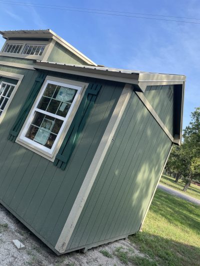 A 10x20 Chalet Shed with green shutters on the side available for sale.