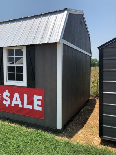 A gray 12x24 Lofted Barn with a sale sign on it, perfect for those looking for sheds on sale or a shed store near them.
