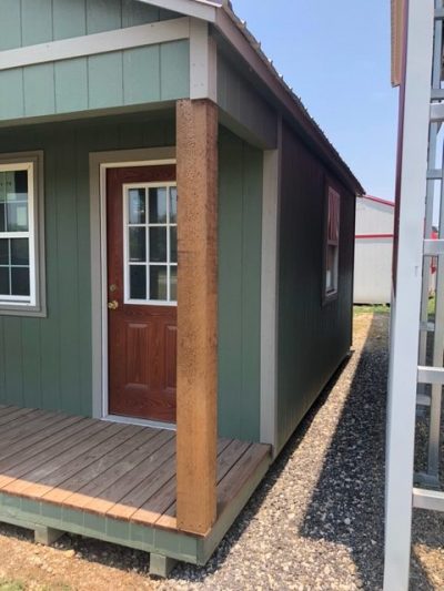 Description: A small green 12x20 Cabinette Shed with a wooden porch available for sale.