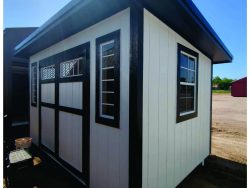 An 8x12 Studio Shed for sale, sitting in the dirt at a shed store near me.