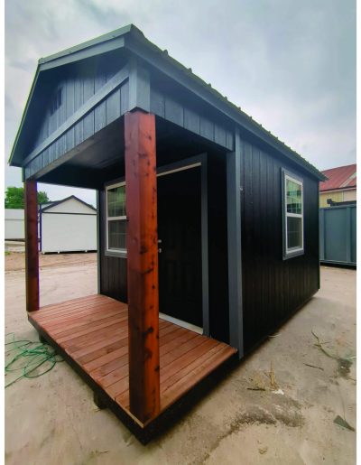 A small black 10x16 Cabinette Shed on sale with a wooden porch.